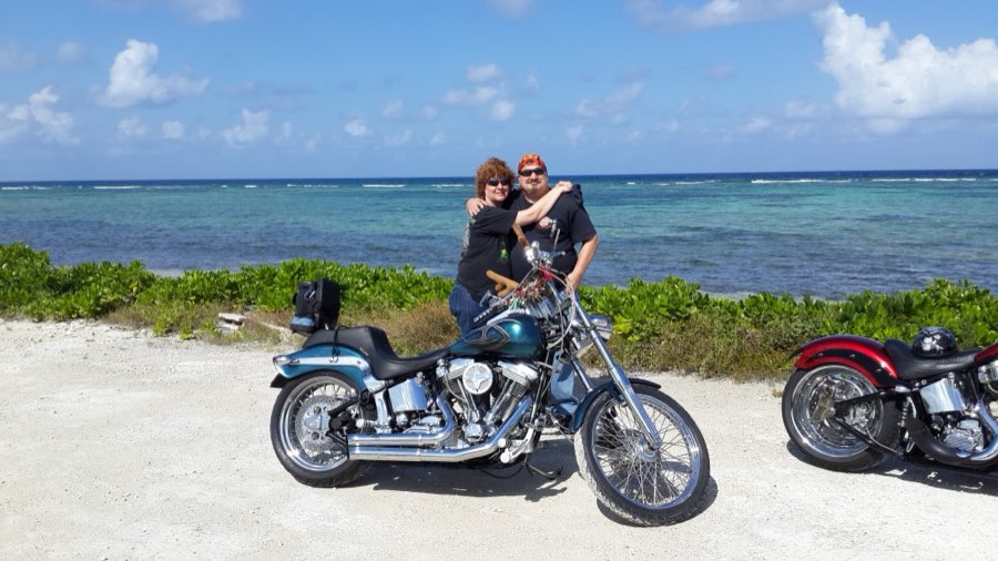 Two guests posing with a custom Harley on a Grand Cayman beach